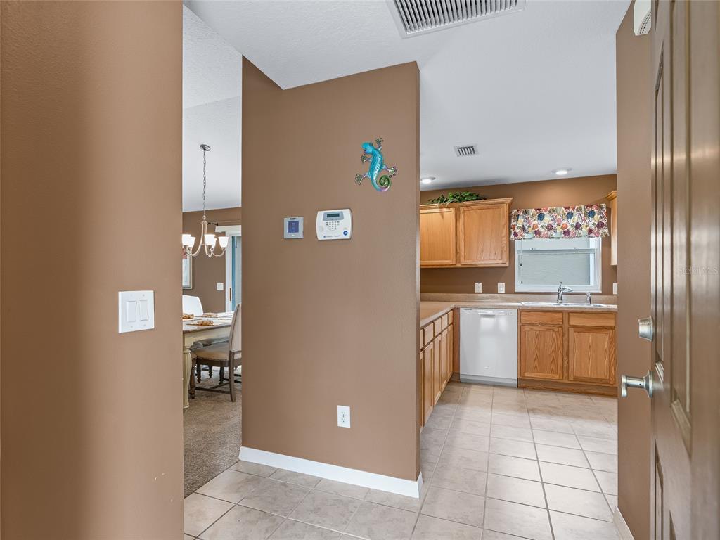 A view from an entryway looking into a kitchen with wood cabinets and tile flooring — 1109 TIPTON LANE, THE VILLAGES, FL