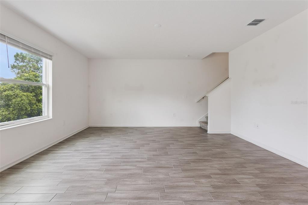 An empty room with wood-look tile flooring, white walls, a window, and a staircase — 33622 SKY BLOSSOM CIRCLE, LEESBURG, FL
