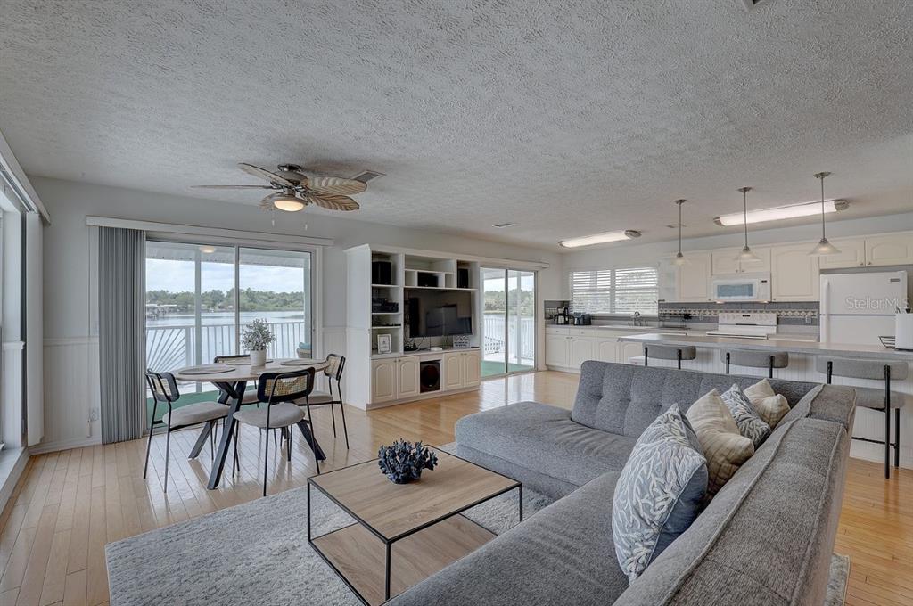 An open-concept living room and kitchen featuring light wood floors, a gray sectional, and waterfront views — 9914 ALAVISTA DRIVE, GIBSONTON, FL