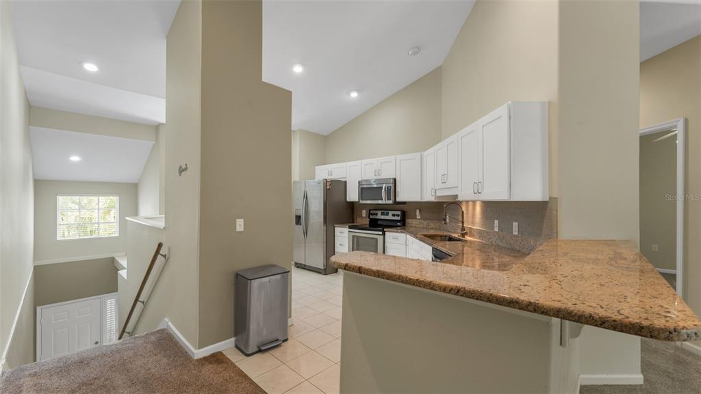 A kitchen with white cabinets, granite countertops, and stainless steel appliances overlooks a carpeted staircase — 386 ENCLAVE DRIVE UNIT 386, LAKELAND, FL