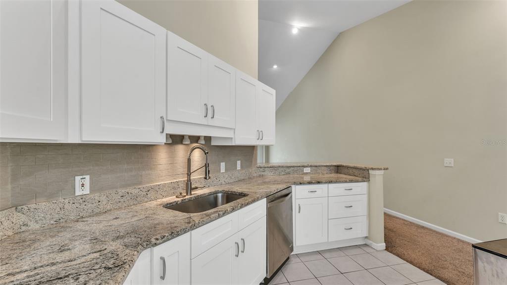 A kitchen features white cabinets, granite countertops, a stainless steel sink, and tile flooring — 386 ENCLAVE DRIVE UNIT 386, LAKELAND, FL