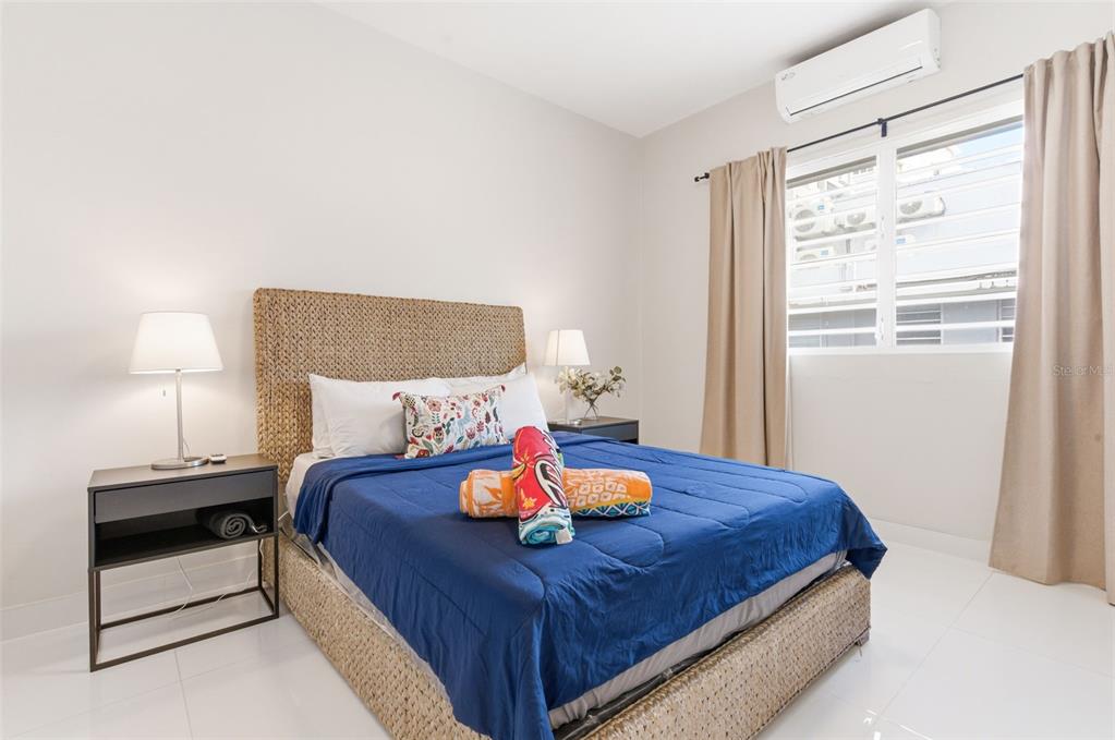 A bedroom features a woven bed frame, a blue comforter, and a window with curtains — 56 CALLE F KRUG CONDADO UNIT PH-1, SAN JUAN, PR