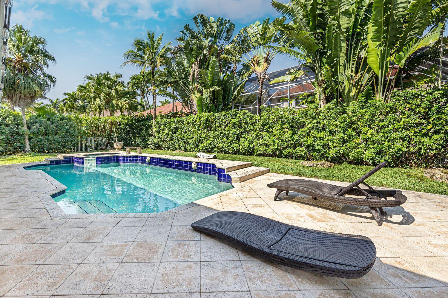 A swimming pool with a tiled deck and two lounge chairs sits in a backyard — 1879 Hidden Trail Lane, Weston FL 33327, WESTON, FL