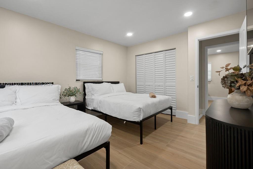 A bedroom features two beds with white linens, light wood-look flooring, and white louvered closet doors — 736 Prosperity Farms Rd, North Palm Beach FL 33408, NORTH PALM BEACH, FL