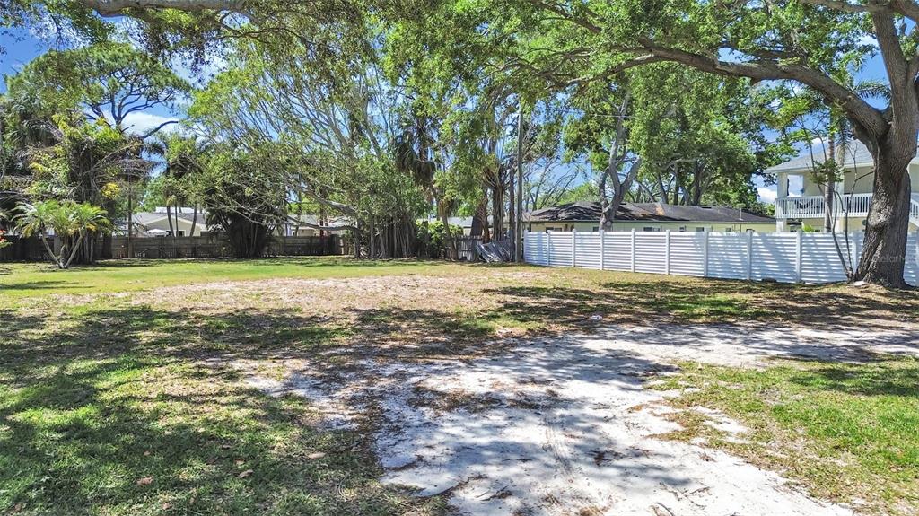 A vacant, grassy lot with sandy patches is bordered by trees and a white fence — 5438 BAYOU GRANDE BOULEVARD NE, ST PETERSBURG, FL