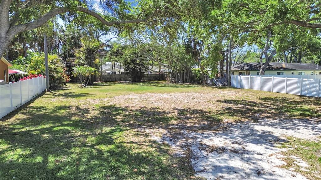 A large, fenced-in grassy lot with mature trees and sandy patches under a blue sky — 5438 BAYOU GRANDE BOULEVARD NE, ST PETERSBURG, FL