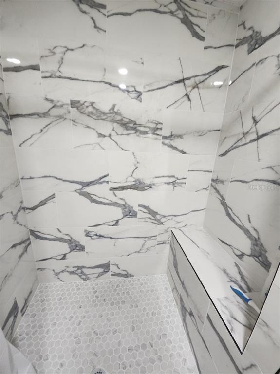 A shower stall features white marble-look wall tiles, a built-in bench, and hexagonal floor tiles — 300 64TH AVENUE UNIT 426, ST PETE BEACH, FL
