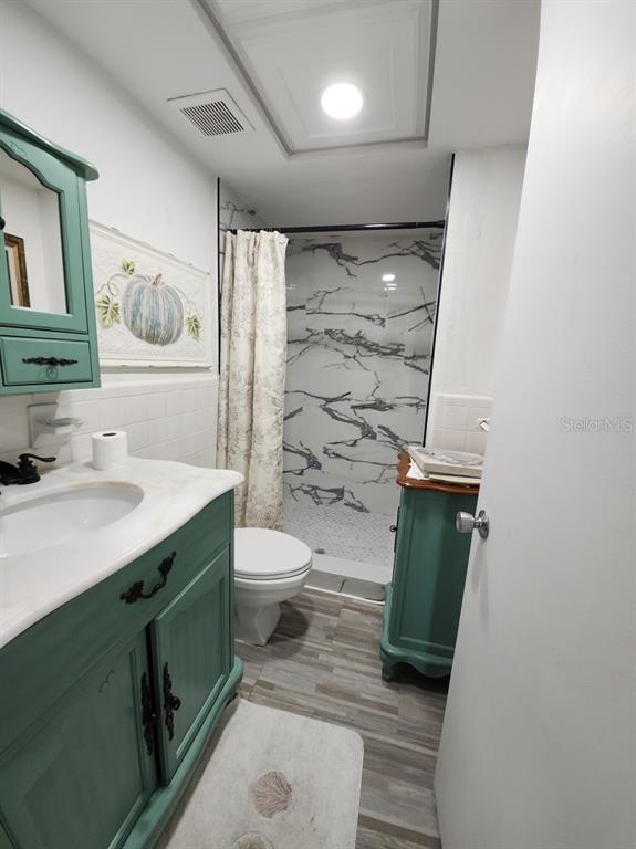 A bathroom features a green vanity, a white toilet, and a walk-in shower with marble-patterned tiles — 300 64TH AVENUE UNIT 426, ST PETE BEACH, FL