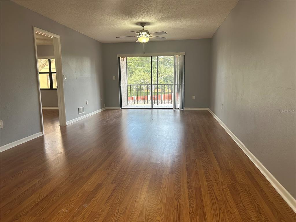 An empty living room with wood-look flooring, gray walls, a ceiling fan, and a balcony — 2971 ESTANCIA BOULEVARD UNIT 321, CLEARWATER, FL