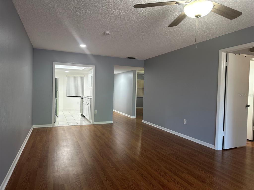 A living room with wood-look flooring, gray walls, and a ceiling fan leads to a kitchen — 2971 ESTANCIA BOULEVARD UNIT 321, CLEARWATER, FL