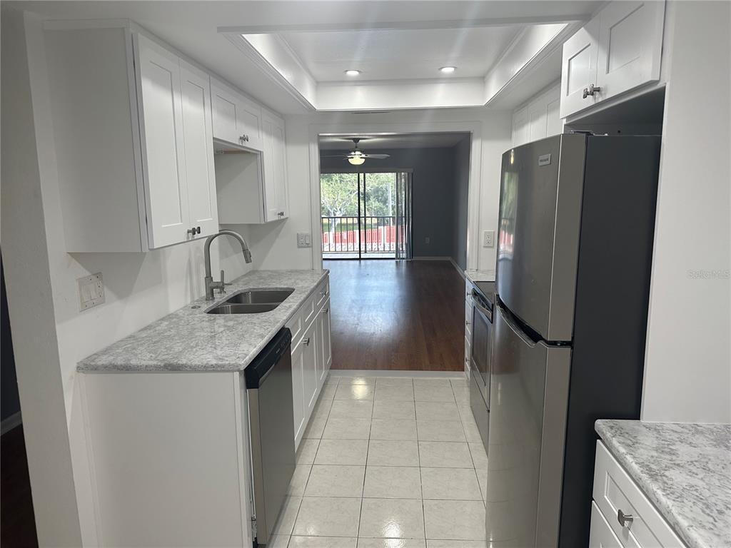 A galley kitchen features white cabinets, granite-look countertops, stainless steel appliances, and tiled flooring — 2971 ESTANCIA BOULEVARD UNIT 321, CLEARWATER, FL