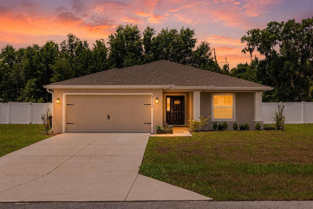 A single-story house with a two-car garage and a concrete driveway at sunset — 9112 SE 41ST COURT ROAD, OCALA, FL