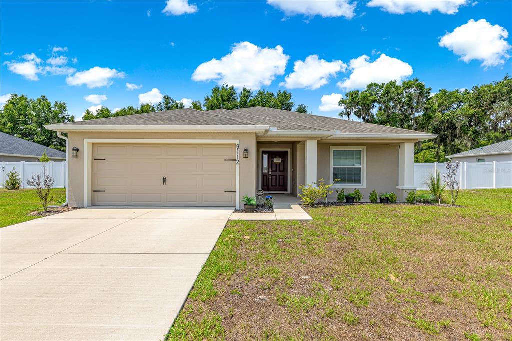 A single-story house with a beige exterior, a two-car garage, and a covered front porch — 9112 SE 41ST COURT ROAD, OCALA, FL