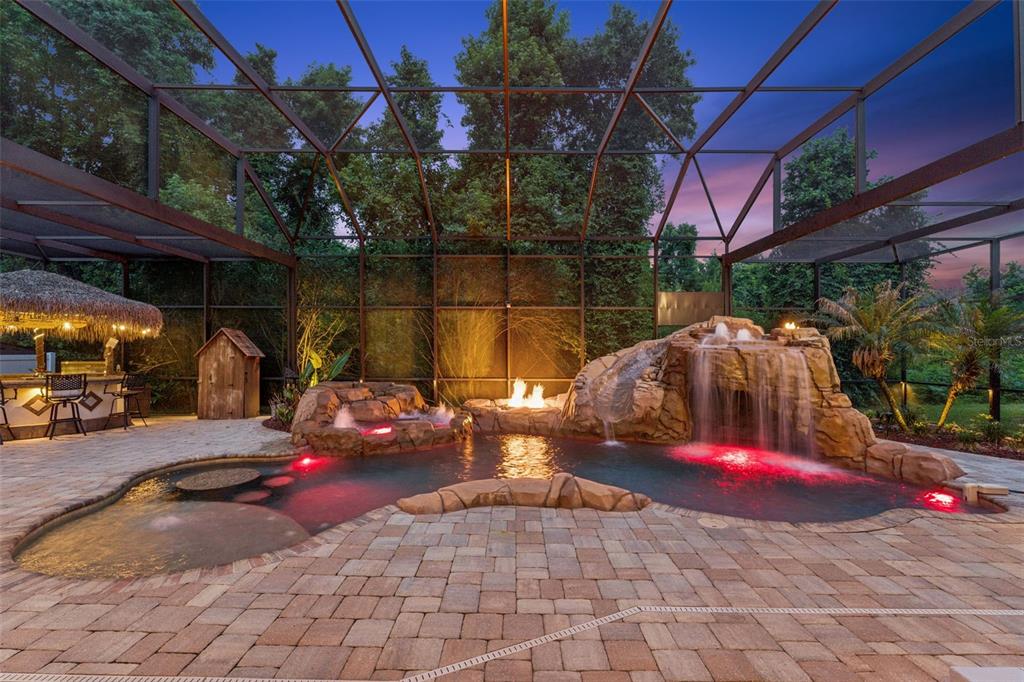 A screened-in pool area features a rock waterfall, fire pit, and a tiki bar — 908 CROTON ROAD, CELEBRATION, FL