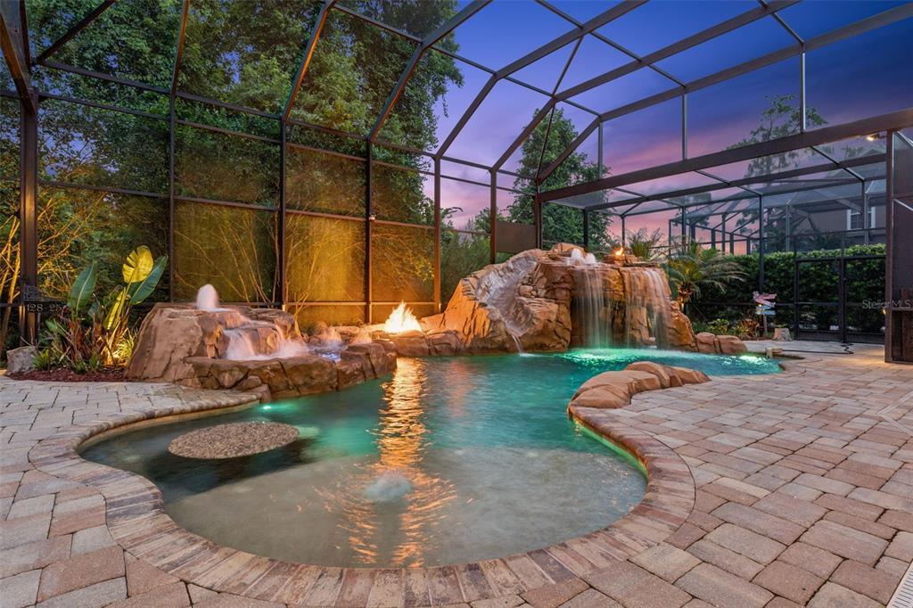 A screened-in swimming pool features a rock waterfall, a slide, and a built-in fire pit — 908 CROTON ROAD, CELEBRATION, FL