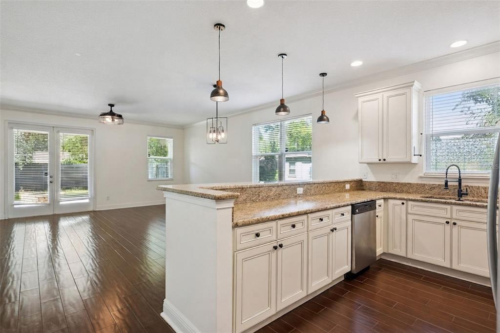 A kitchen with white cabinets and granite countertops overlooks a living area with wood floors — 2806 KILGORE STREET, ORLANDO, FL
