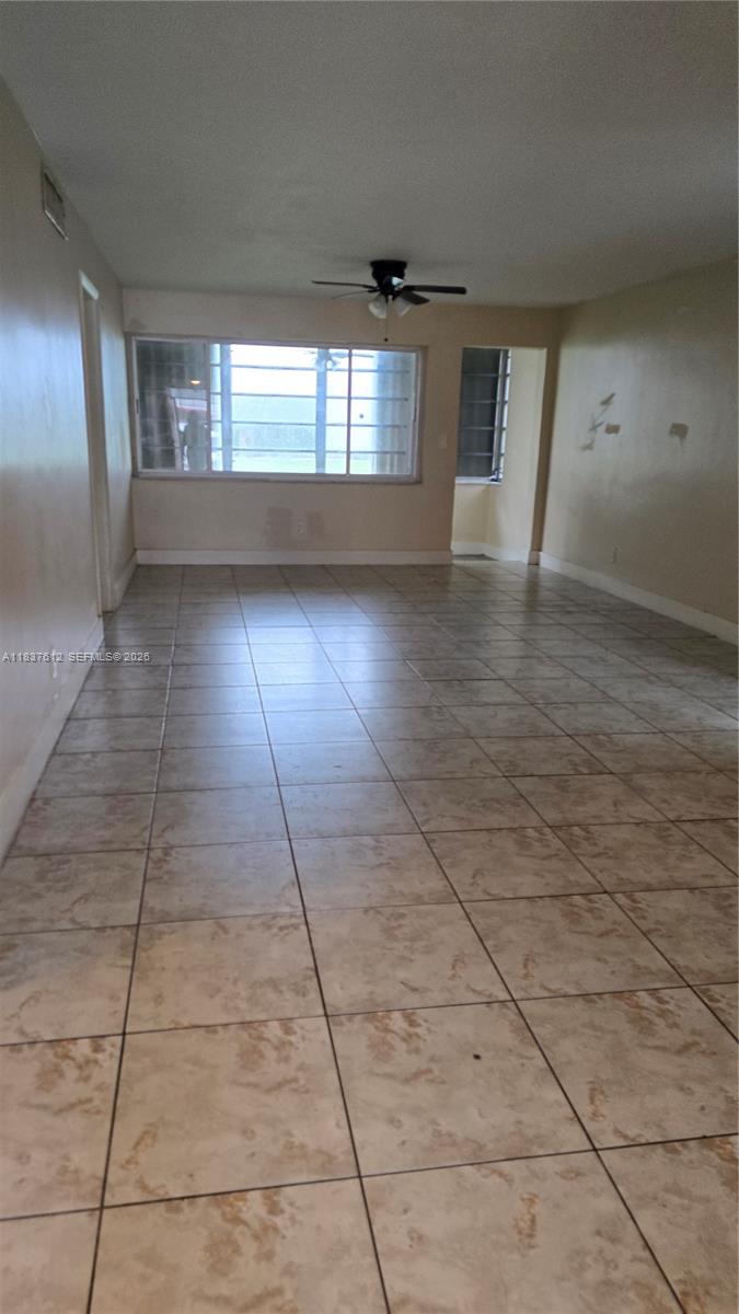 An empty room features beige tile flooring, a ceiling fan, and a large window — 1450 NE 191st St # 106, Miami FL 33179, MIAMI, FL