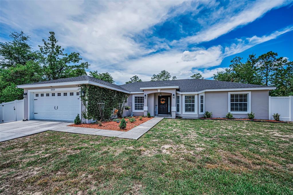 A single-story house with a two-car garage, light-colored stucco exterior, and a grassy front yard — 12123 FULMAR ROAD, WEEKI WACHEE, FL