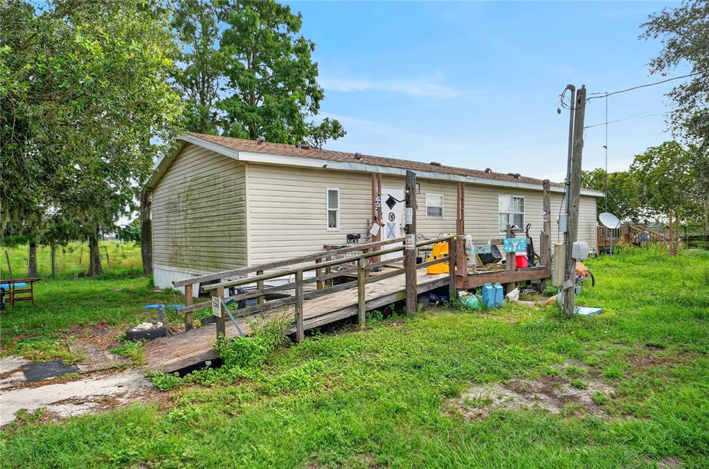 A single-story mobile home with tan siding and a wooden wheelchair ramp leading to the entrance — 56 MEADOW WAY, FROSTPROOF, FL