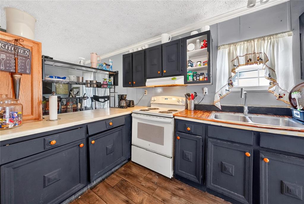A kitchen features dark blue cabinets with orange knobs, a white stove, and wood flooring — 56 MEADOW WAY, FROSTPROOF, FL