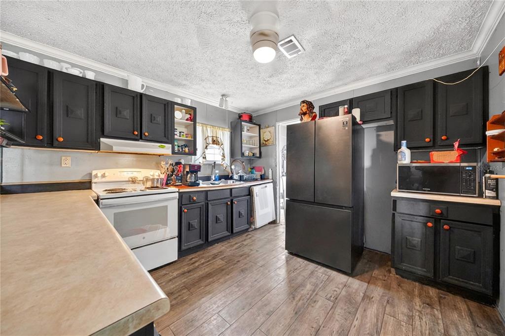 A kitchen features black cabinets, a white stove, a black refrigerator, and wood-look flooring — 56 MEADOW WAY, FROSTPROOF, FL