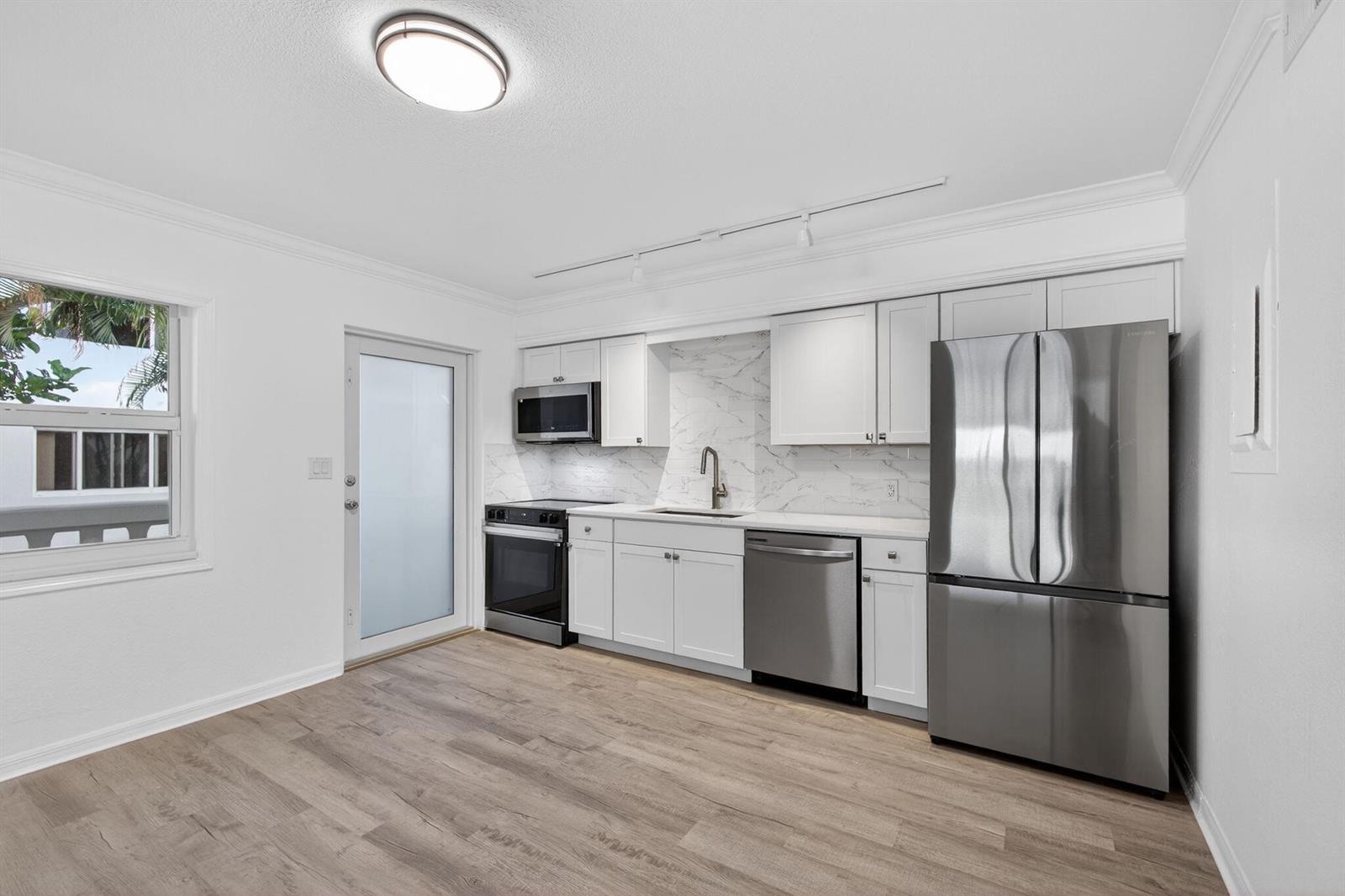 A kitchen features white cabinets, marble-look backsplash, stainless steel appliances, and light wood-look flooring — 624 Southwind Circle # 4, North Palm Beach FL 33408, NORTH PALM BEACH, FL
