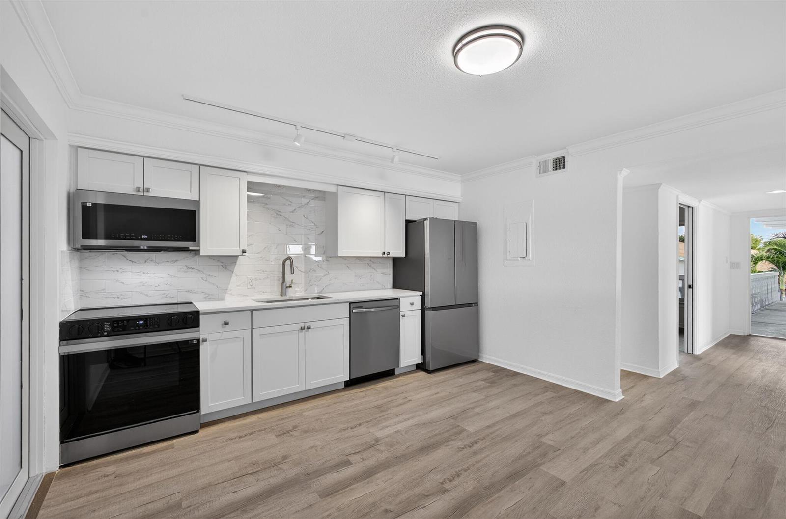 A modern kitchen features white cabinets, stainless steel appliances, and light wood-look flooring — 624 Southwind Circle # 4, North Palm Beach FL 33408, NORTH PALM BEACH, FL