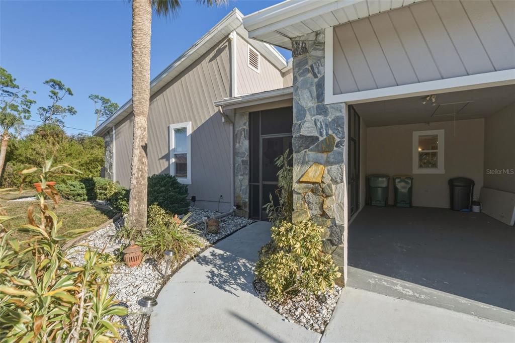 A concrete walkway leads to a screened front entrance beside a stone-accented carport — 643 BLUE LANE NW, PORT CHARLOTTE, FL