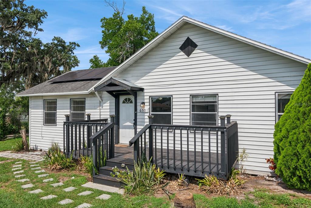 A white house with horizontal siding features a dark wooden deck and a front entrance — 650 S LAKEWOOD AVENUE, OCOEE, FL