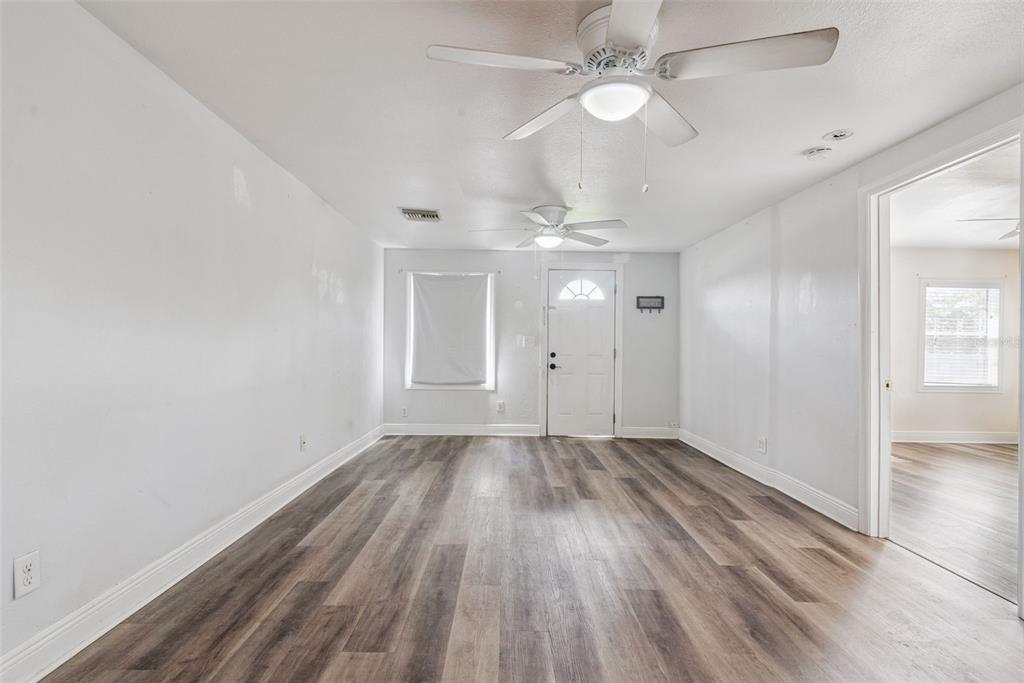 An empty room features white walls, wood-look flooring, two ceiling fans, and a front door — 650 S LAKEWOOD AVENUE, OCOEE, FL