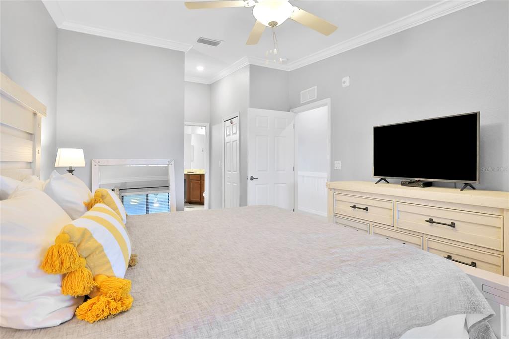 A bedroom features a bed with yellow pillows, a dresser with a television, and ceiling fan — 5634 PALMER CIRCLE UNIT 203, BRADENTON, FL