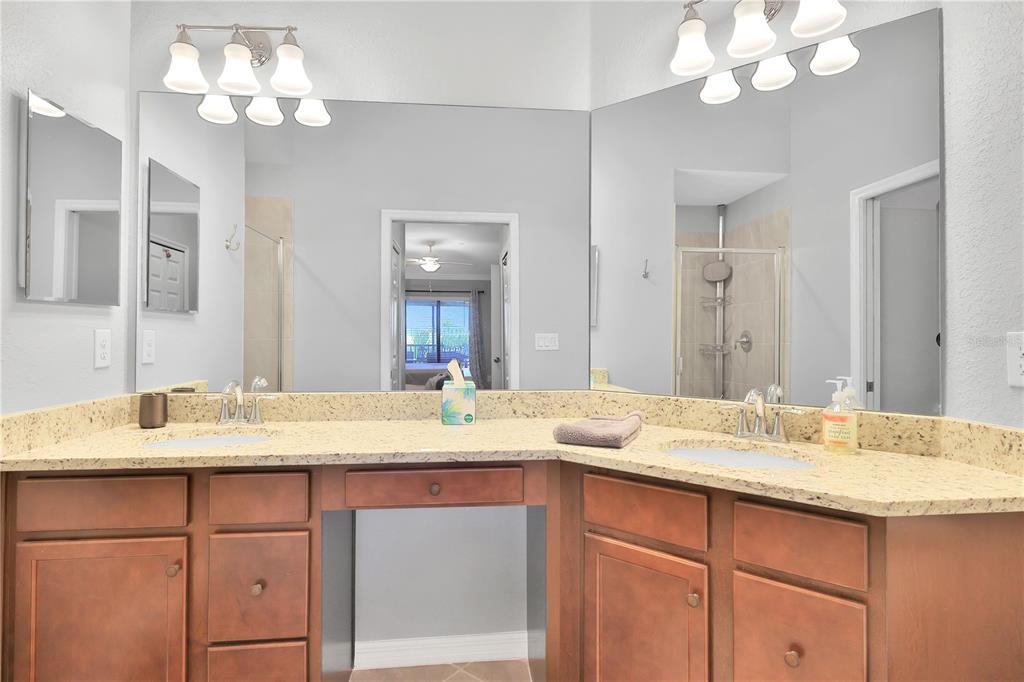 A bathroom features a dual-sink vanity with granite countertops, wood cabinets, and large wall mirrors — 5634 PALMER CIRCLE UNIT 203, BRADENTON, FL