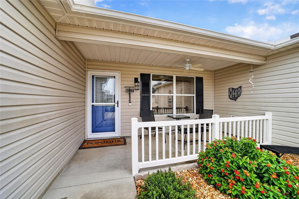 A covered front porch features beige vinyl siding, a white railing, and a blue door — 940 EASTMONT COURT, THE VILLAGES, FL