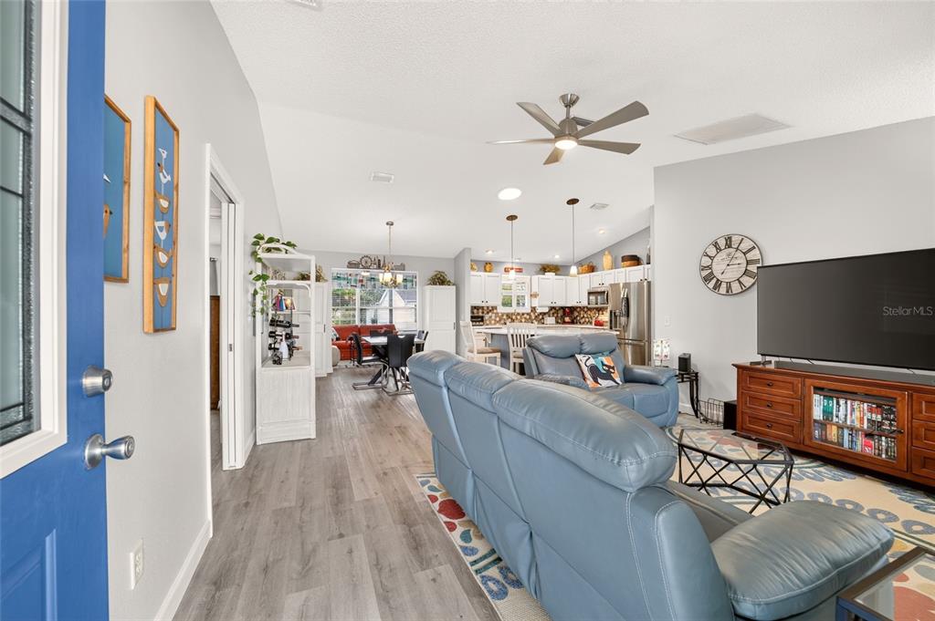 An open-concept living room and kitchen featuring light wood-look flooring and blue leather furniture — 940 EASTMONT COURT, THE VILLAGES, FL