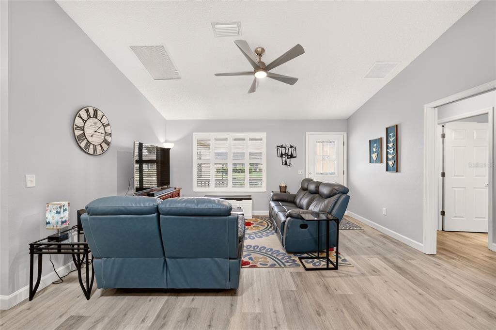 A living room features light gray walls, wood-look flooring, two blue sofas, and a ceiling fan — 940 EASTMONT COURT, THE VILLAGES, FL