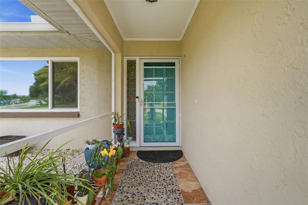 A covered entryway features a teal screen door, a pebble-tiled walkway, and potted plants — 290 CAPRI AVENUE, VENICE, FL