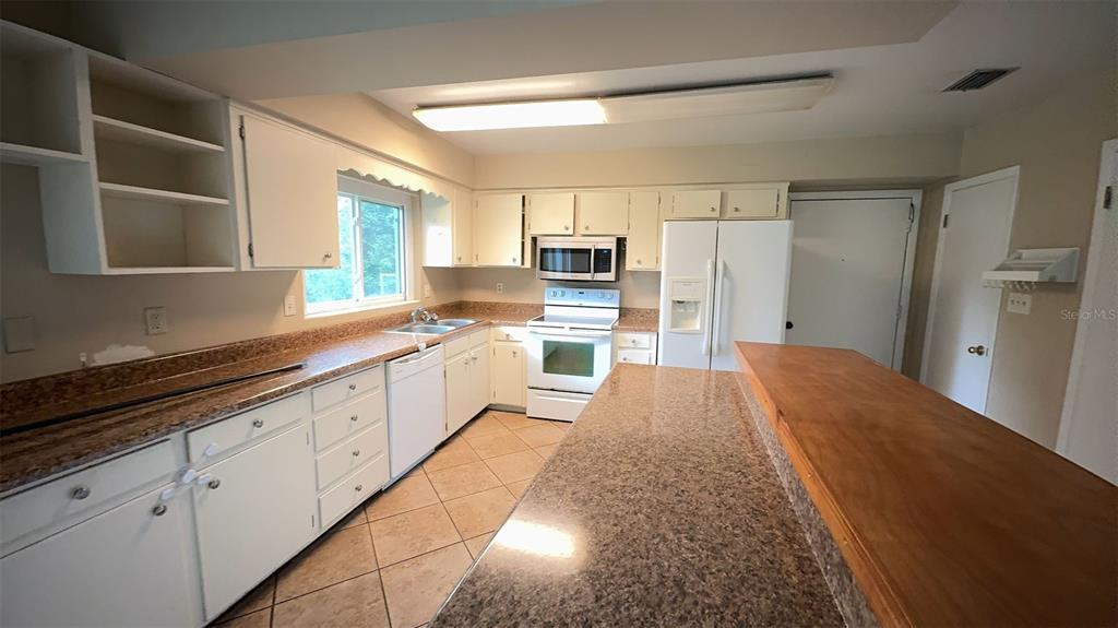 A kitchen features white cabinets, granite countertops, a breakfast bar, and tile flooring — 3330 NW 27TH AVENUE, GAINESVILLE, FL