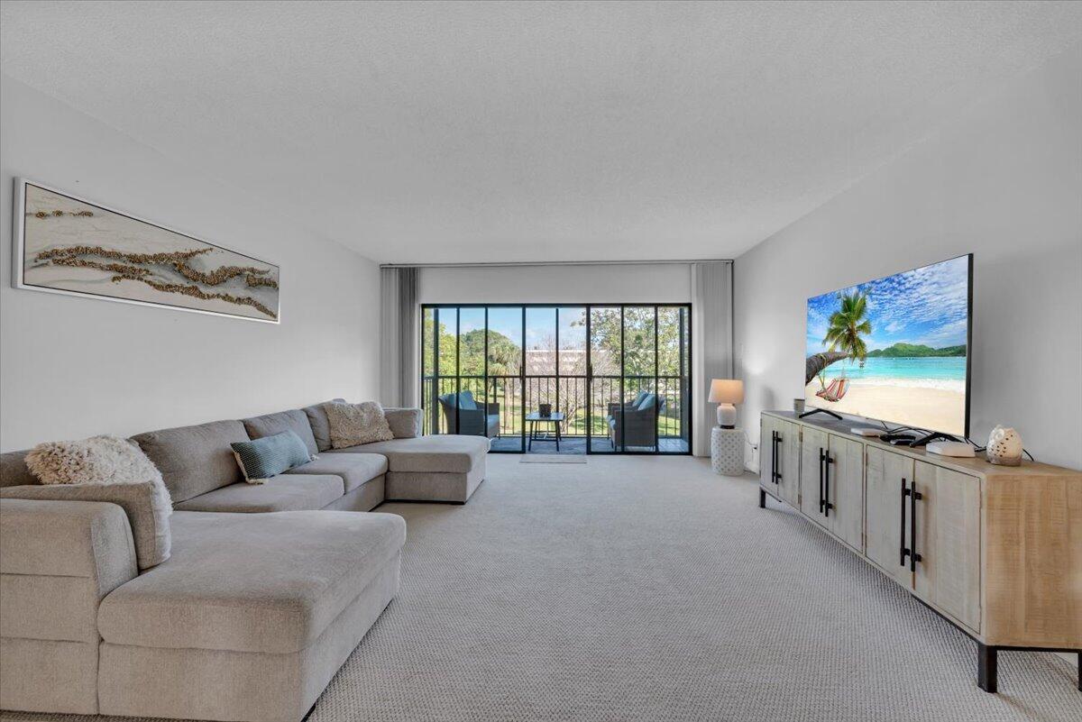A living room features a gray sectional sofa, a media console, and a sliding glass door — 300 N Highway A1a # 304h, Jupiter FL 33477, JUPITER, FL
