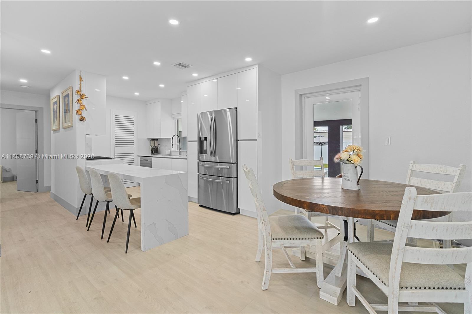 A modern kitchen features white cabinetry, a marble-topped island, and a wooden dining table — 11350 SW 57th St, Miami FL 33173, MIAMI, FL