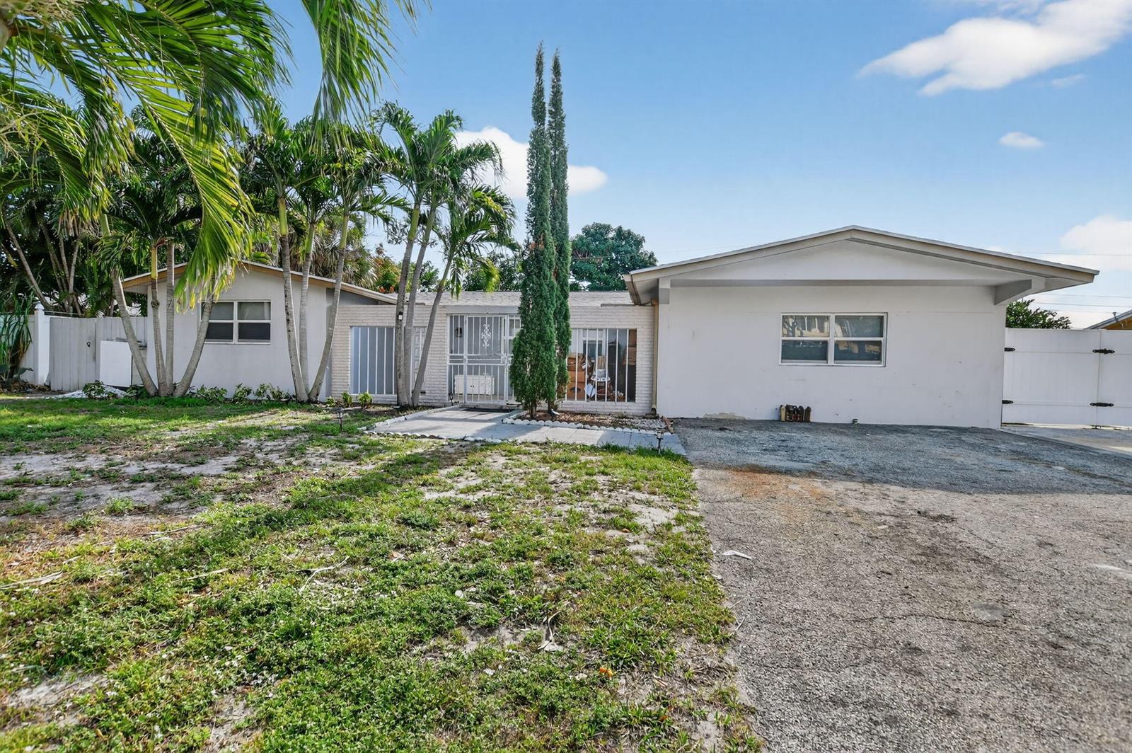 A single-story house with a gravel driveway, white exterior, and tall cypress trees in front — 256 SW 11th Place, Boca Raton FL 33432, BOCA RATON, FL