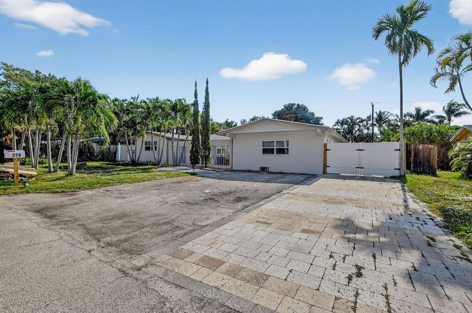 A white single-story house features a paved driveway, a large gate, and several palm trees — 256 SW 11th Place, Boca Raton FL 33432, BOCA RATON, FL