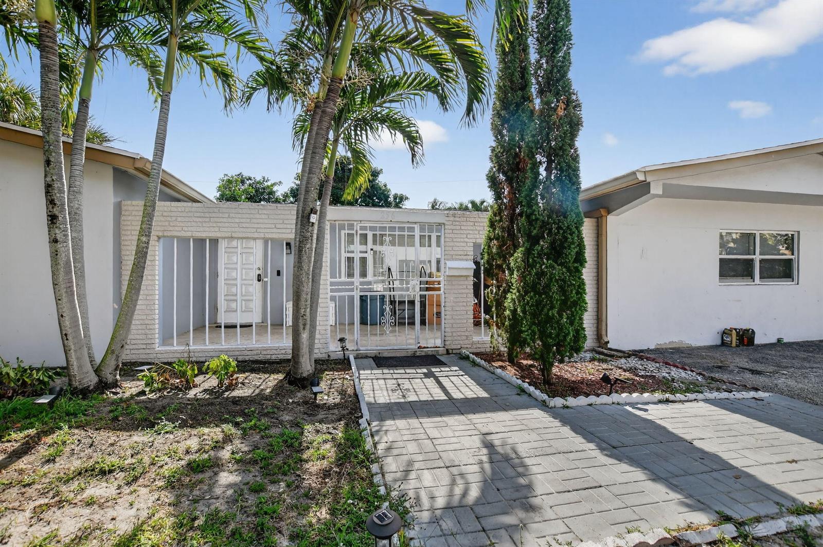 A white brick house exterior features a gated courtyard, palm trees, and a paved walkway — 256 SW 11th Place, Boca Raton FL 33432, BOCA RATON, FL