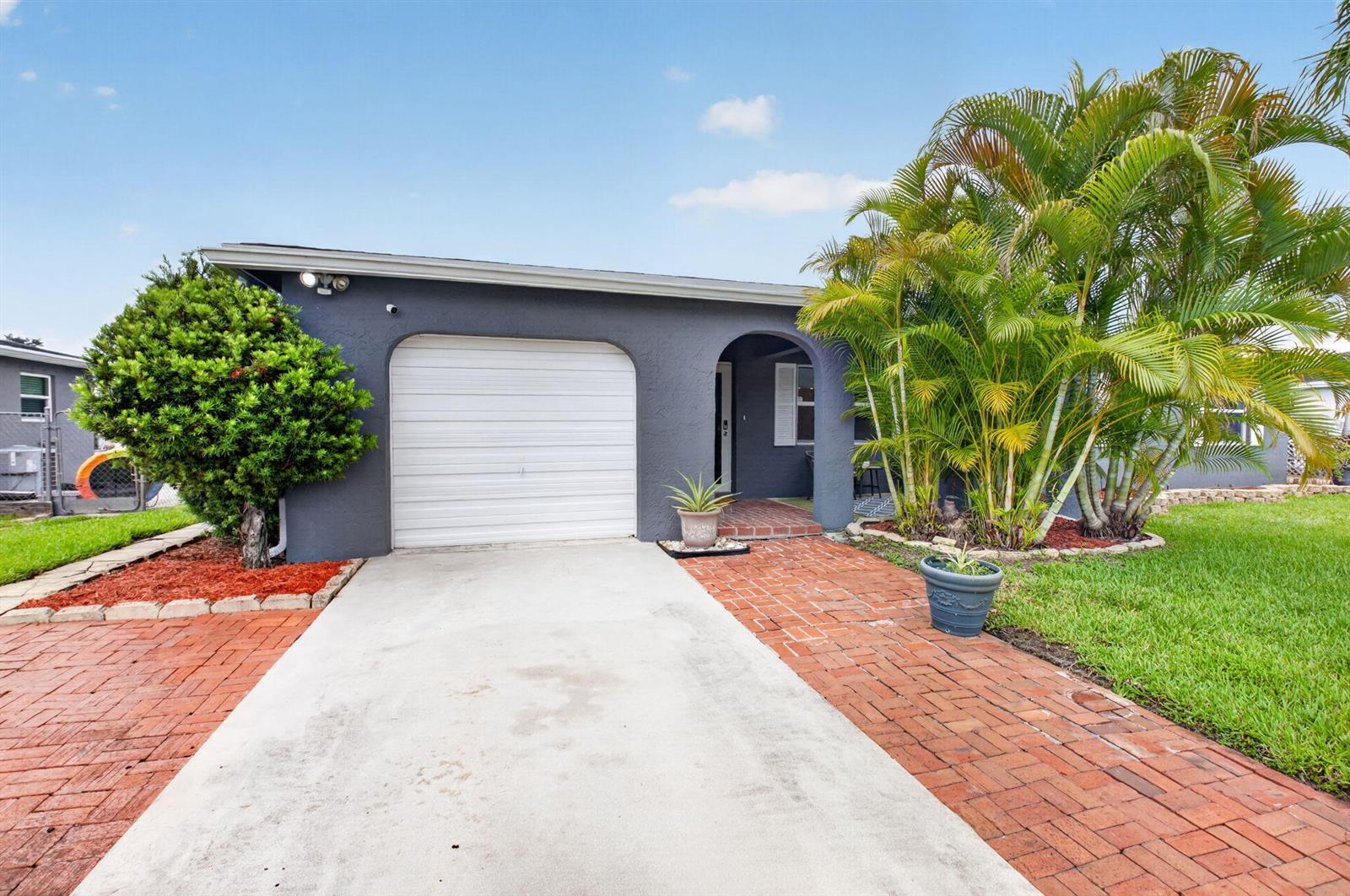 A gray house with a white garage door, brick walkway, and palm trees in the yard — 4599 Betelnut Street, Boca Raton FL 33428, BOCA RATON, FL