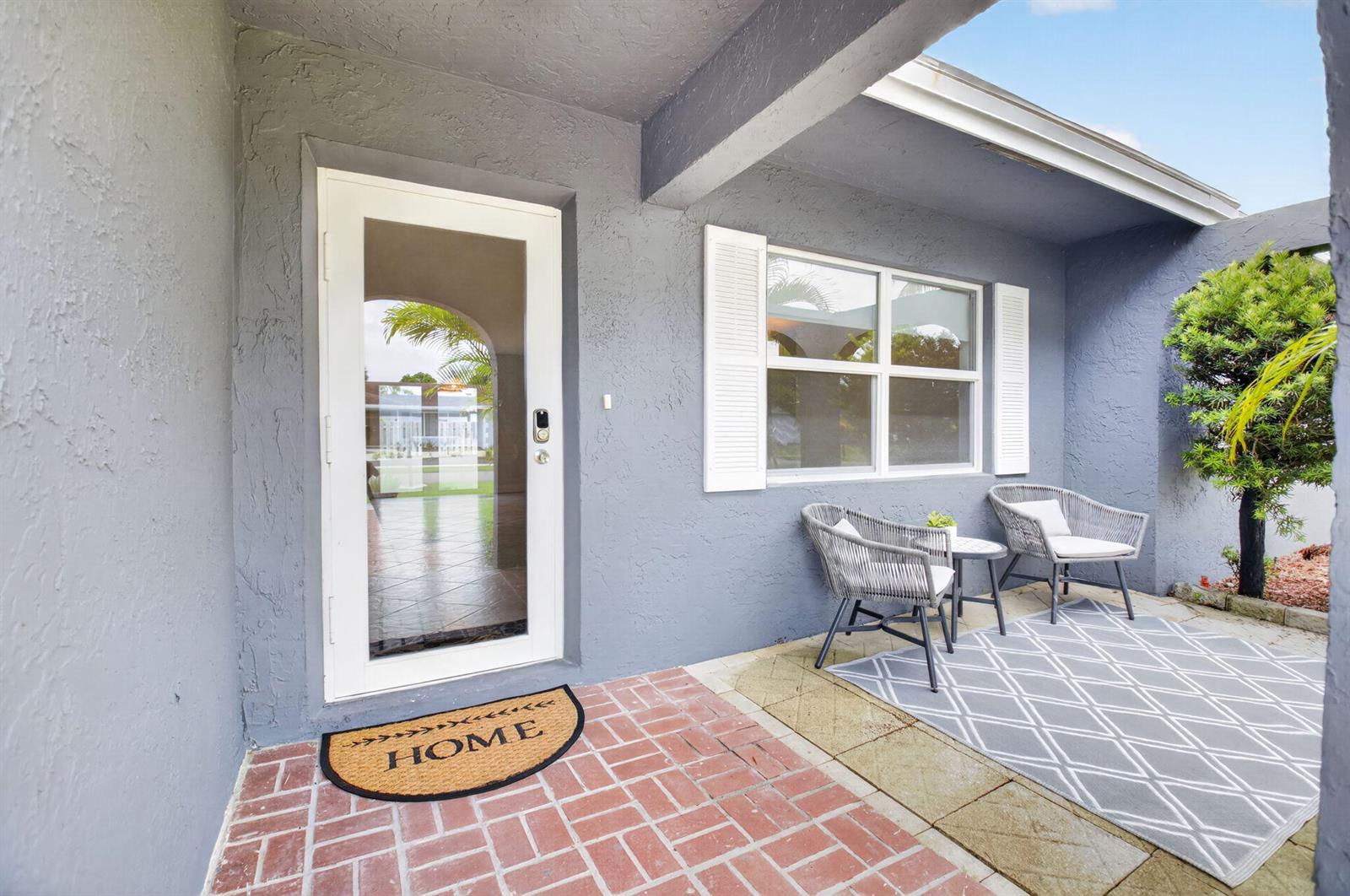 A gray exterior entryway features a white front door, a window with shutters, and seating — 4599 Betelnut Street, Boca Raton FL 33428, BOCA RATON, FL