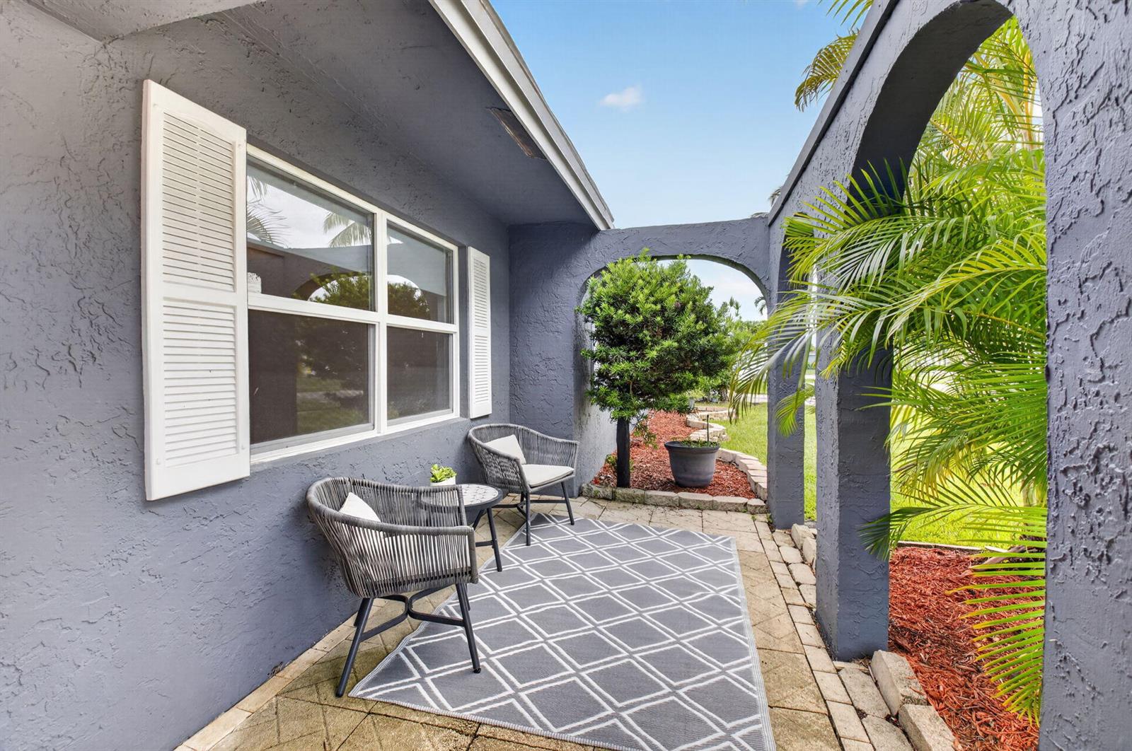 A gray stucco patio features two woven chairs, a small table, and a geometric rug — 4599 Betelnut Street, Boca Raton FL 33428, BOCA RATON, FL