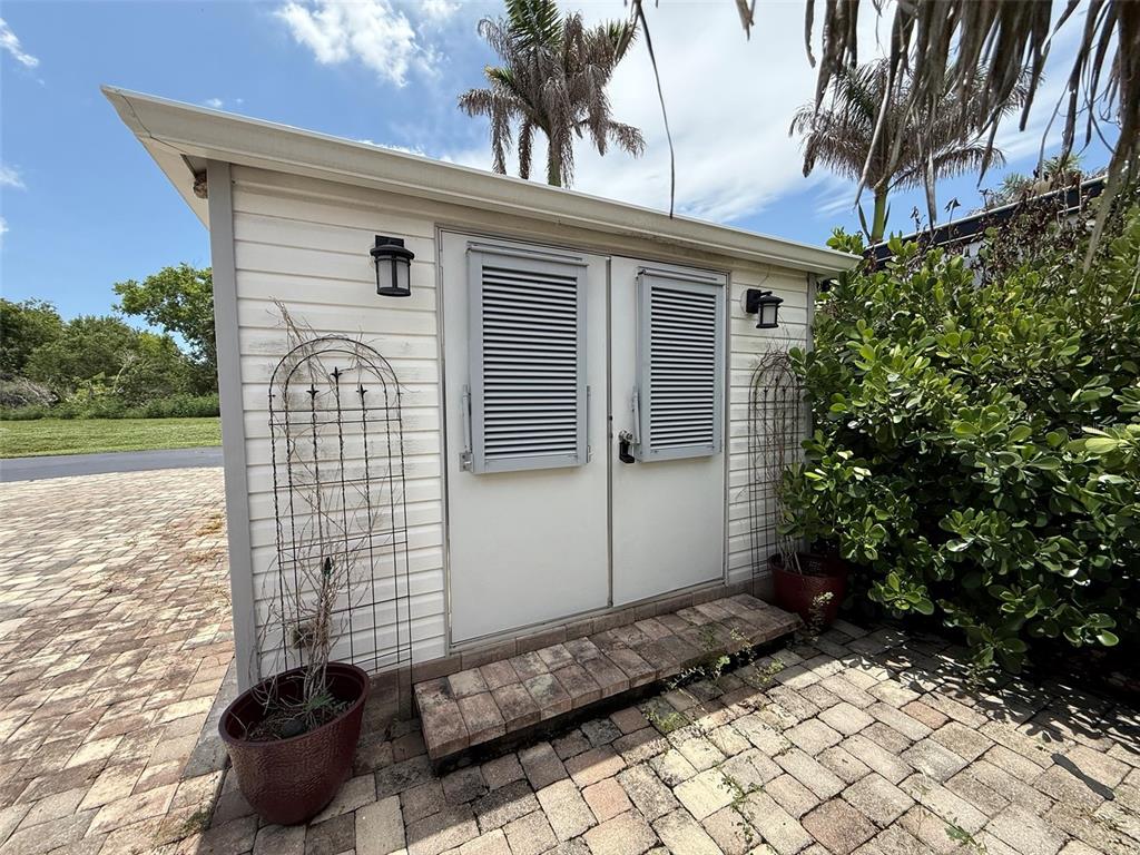 A small, light-colored shed with double doors and louvered shutters sits on a brick patio — 3520 SW 7TH MANOR UNIT 357, OKEECHOBEE, FL