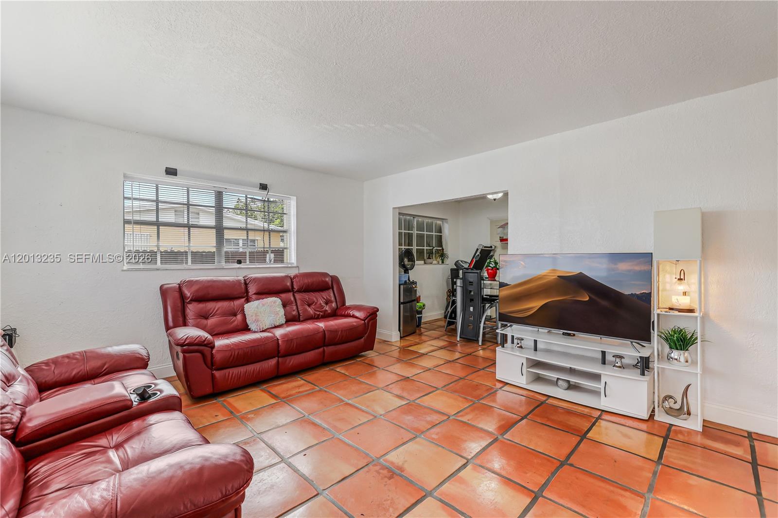 A living room features red leather sofas, a television on a stand, and terracotta flooring — 11600 SW 181st Ter, Miami FL 33157, MIAMI, FL