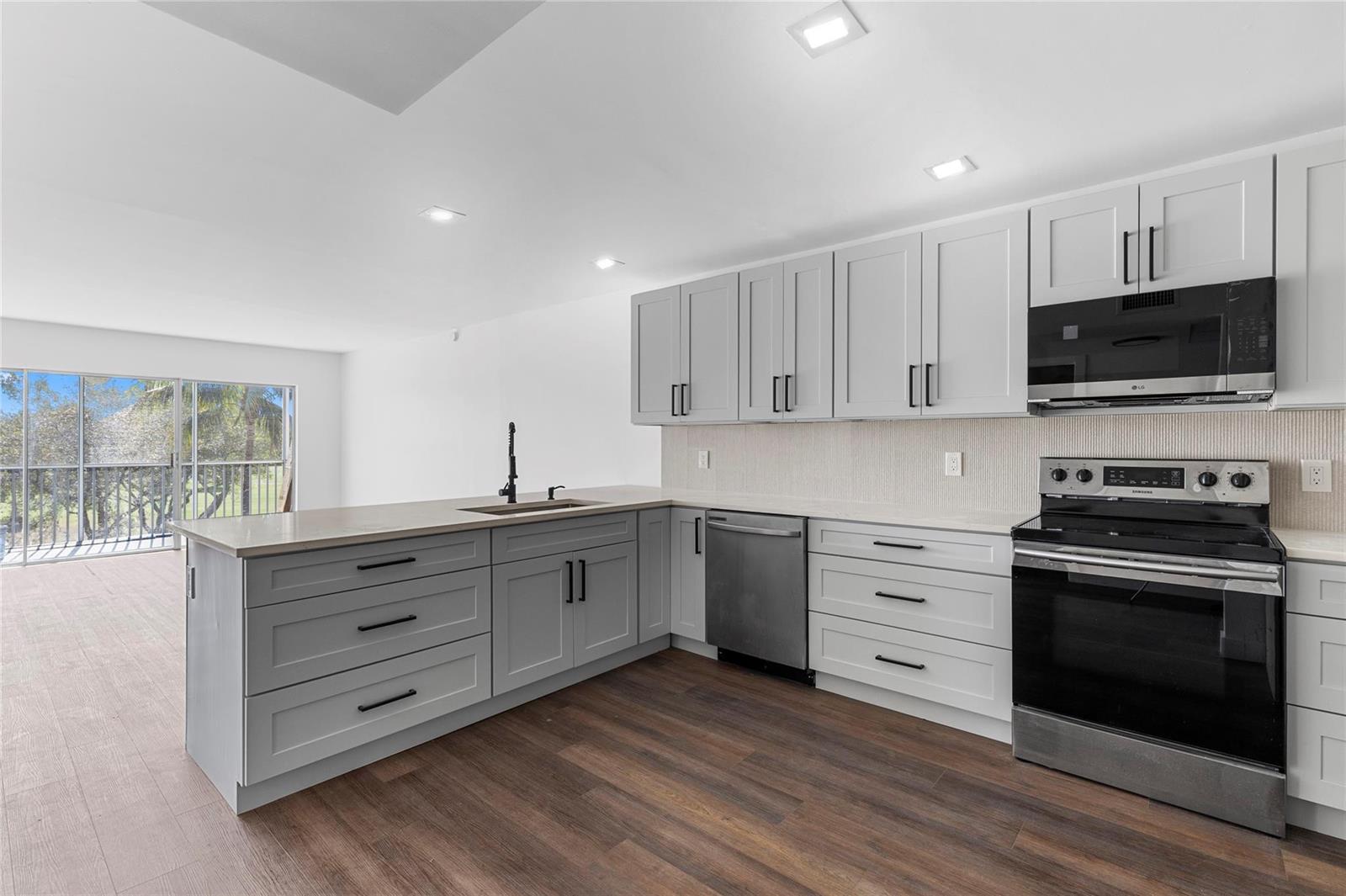 A modern kitchen features grey cabinets, stainless steel appliances, and a view of a balcony — 2800 N Palm Aire Drive # 310, Pompano Beach FL 33069, POMPANO BEACH, FL