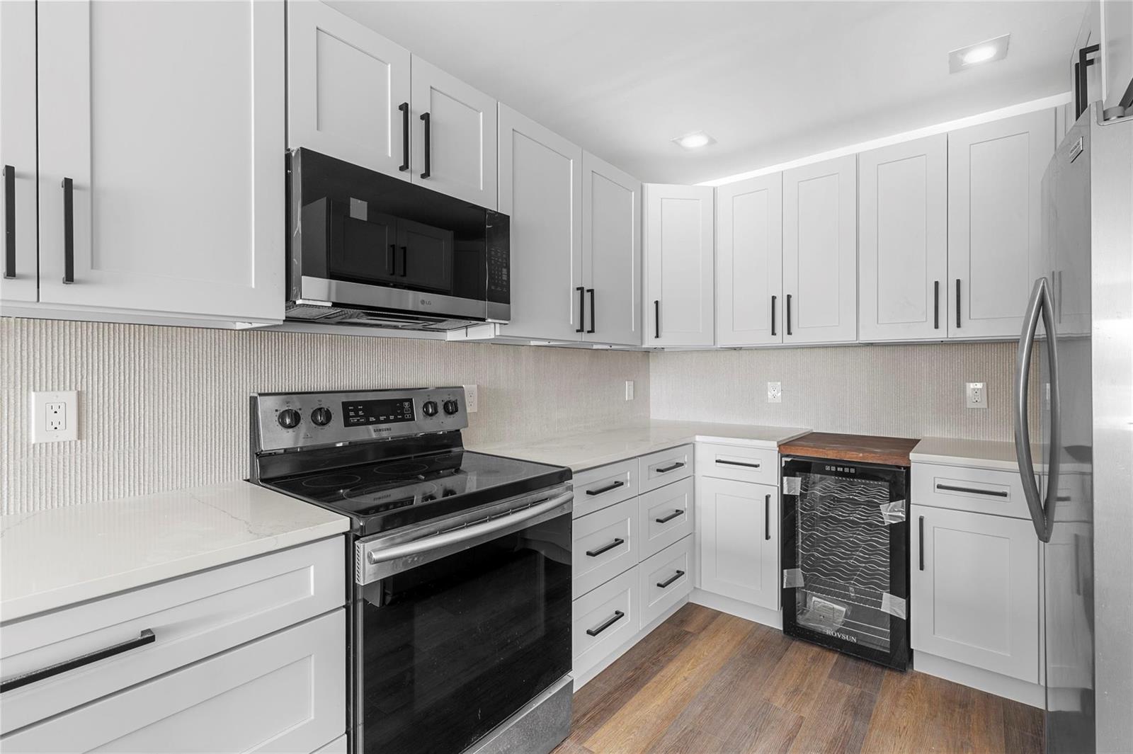A modern kitchen features white cabinets, stainless steel appliances, a wine cooler, and light countertops — 2800 N Palm Aire Drive # 310, Pompano Beach FL 33069, POMPANO BEACH, FL