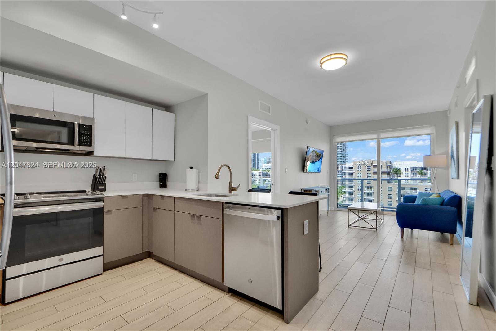 A modern kitchen with white and gray cabinetry opens into a living area with balcony — 321 NE 26th St # 806, Miami FL 33137, MIAMI, FL
